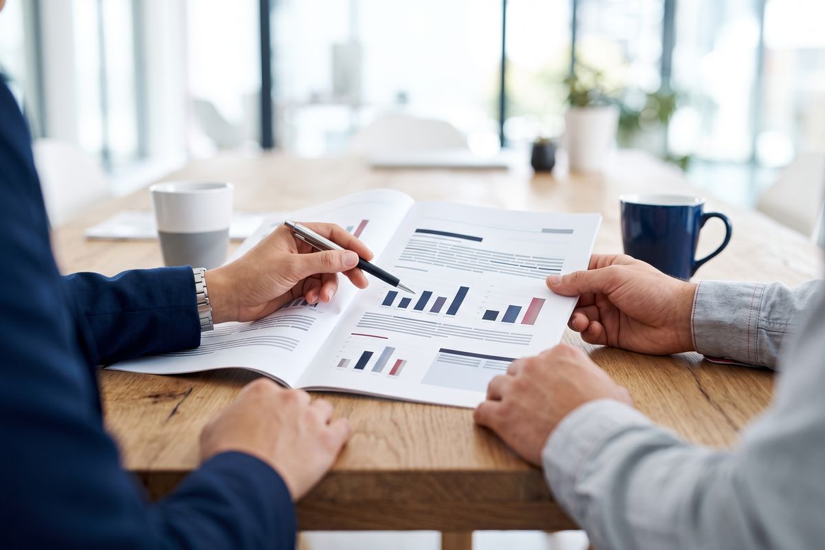 Business owner and consultant reviewing a printed safety report at a table, seen from the shoulders down